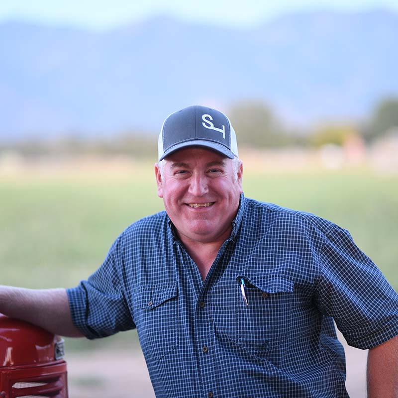 Man wearing a blue cap with a logo, smiling outdoors.