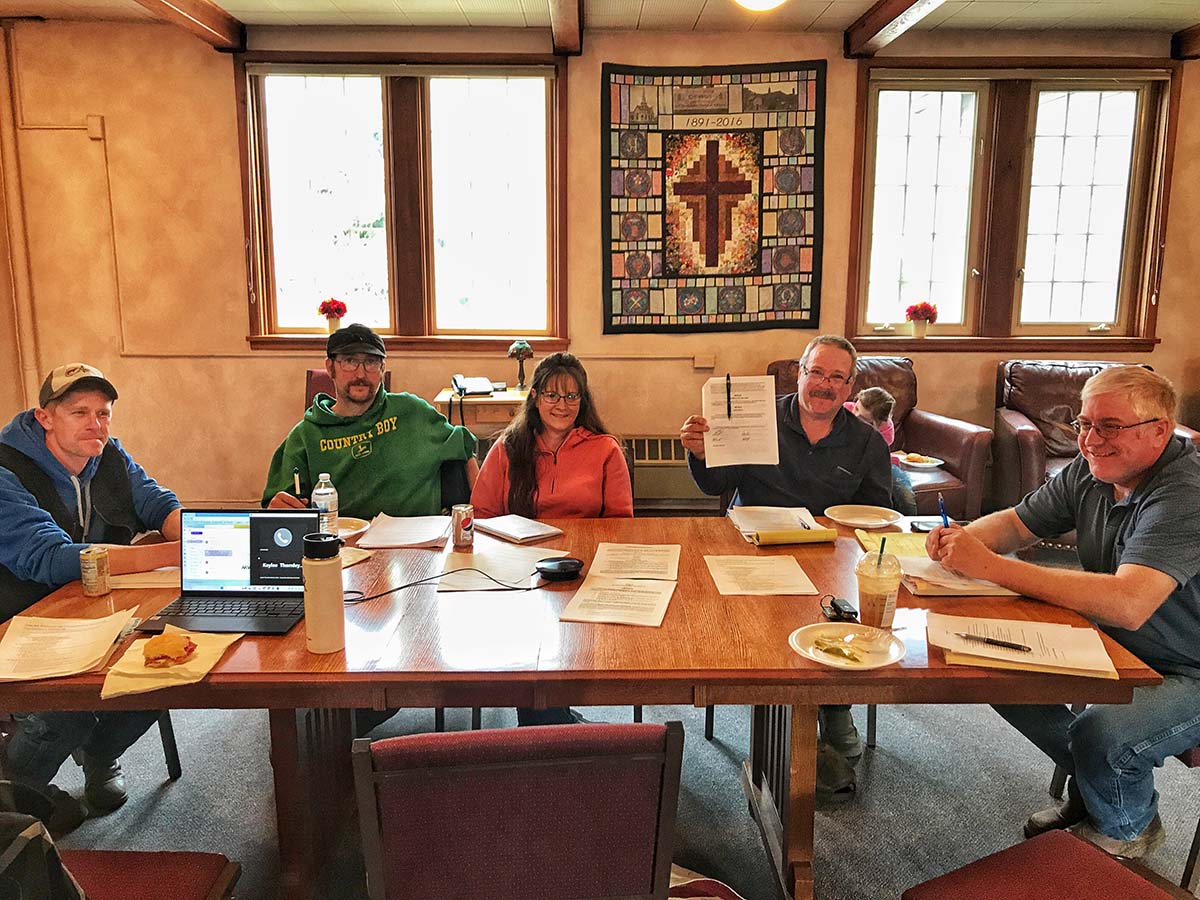 Group of people sitting around a table in a room, signing the articles for Glacier Processing Cooperative.