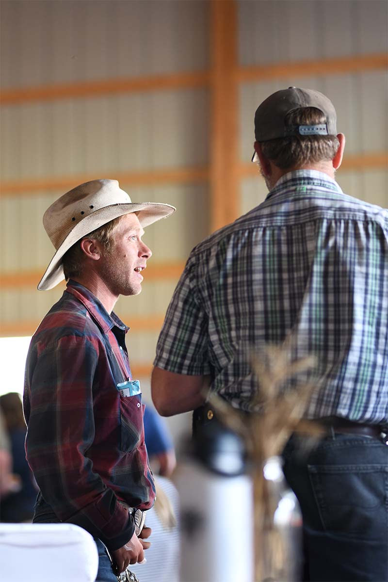 Two men in plaid shirts and cowboy hats standing indoors.