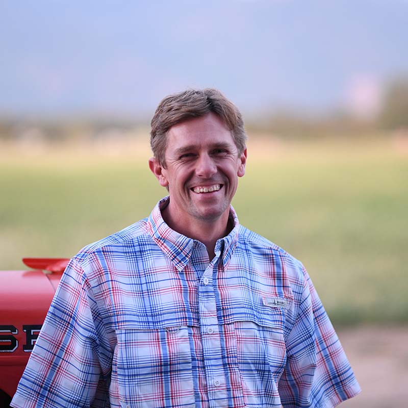 Man wearing a plaid shirt standing in front of a blurred outdoor background