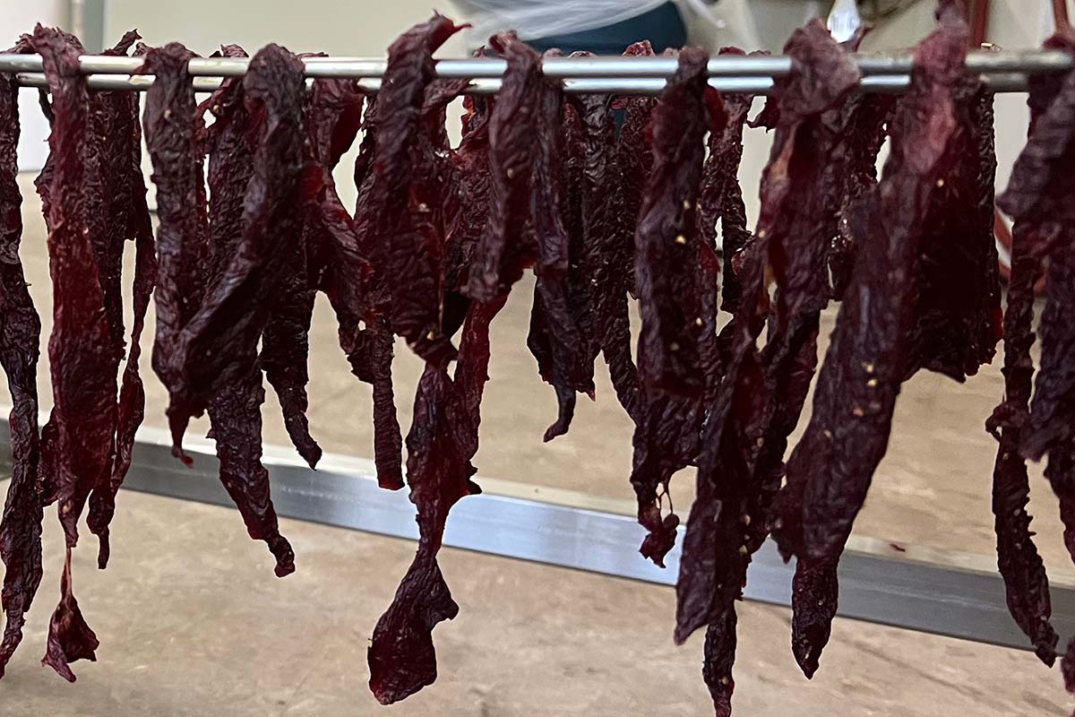 Dried meat strips hanging on a metal rod against a neutral background