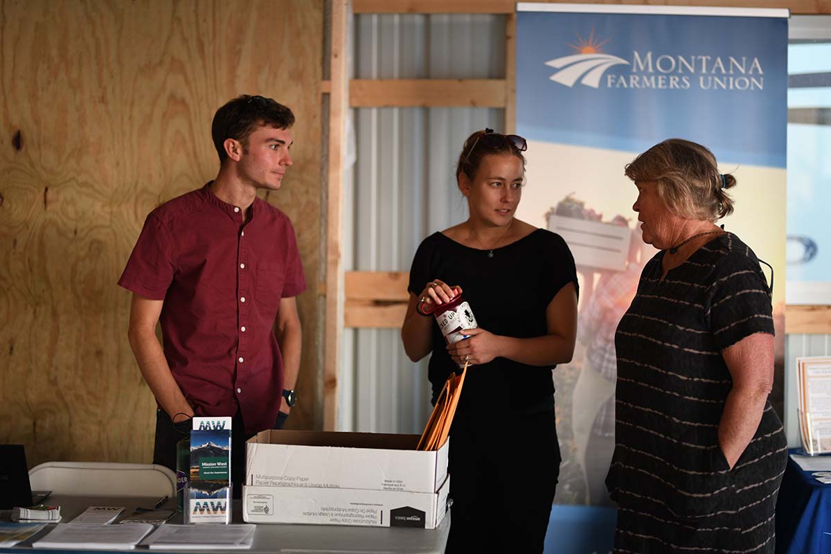 Three people standing near a table with a Montana Farmers Union banner in the background.