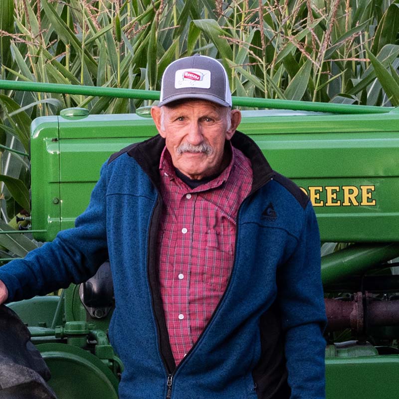 Man standing in front of a green John Deere tractor in a field.